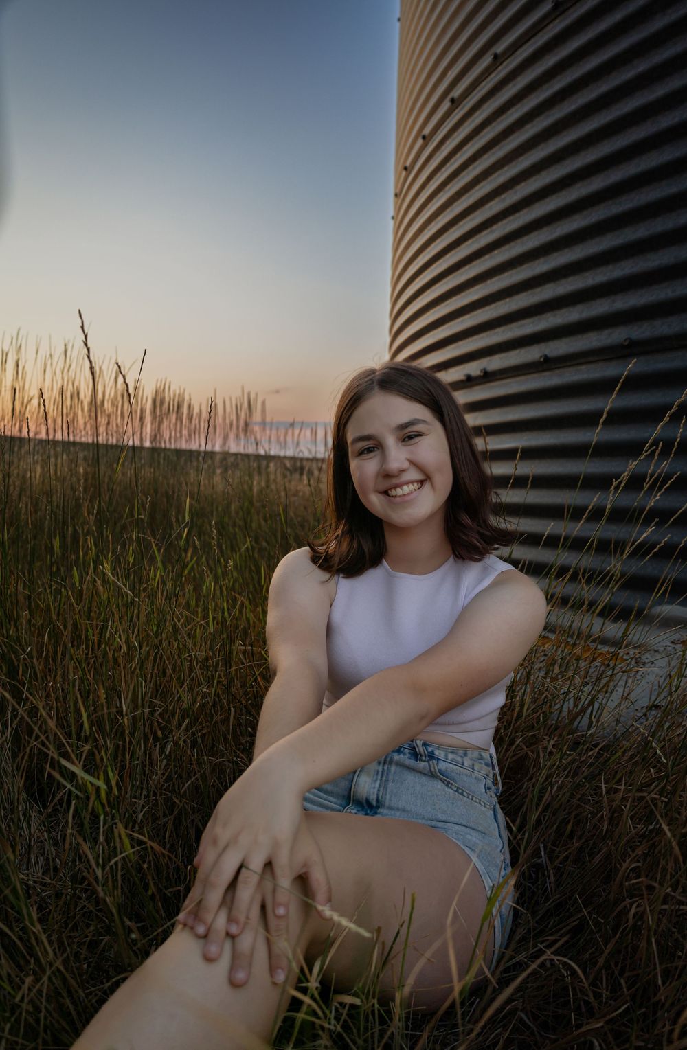 Relaxed outdoor photo session near metal grain silo at dusk.