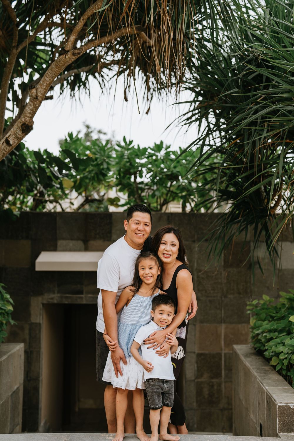 A family shares joyful moments together on outdoor steps surrounded by tropical plants.