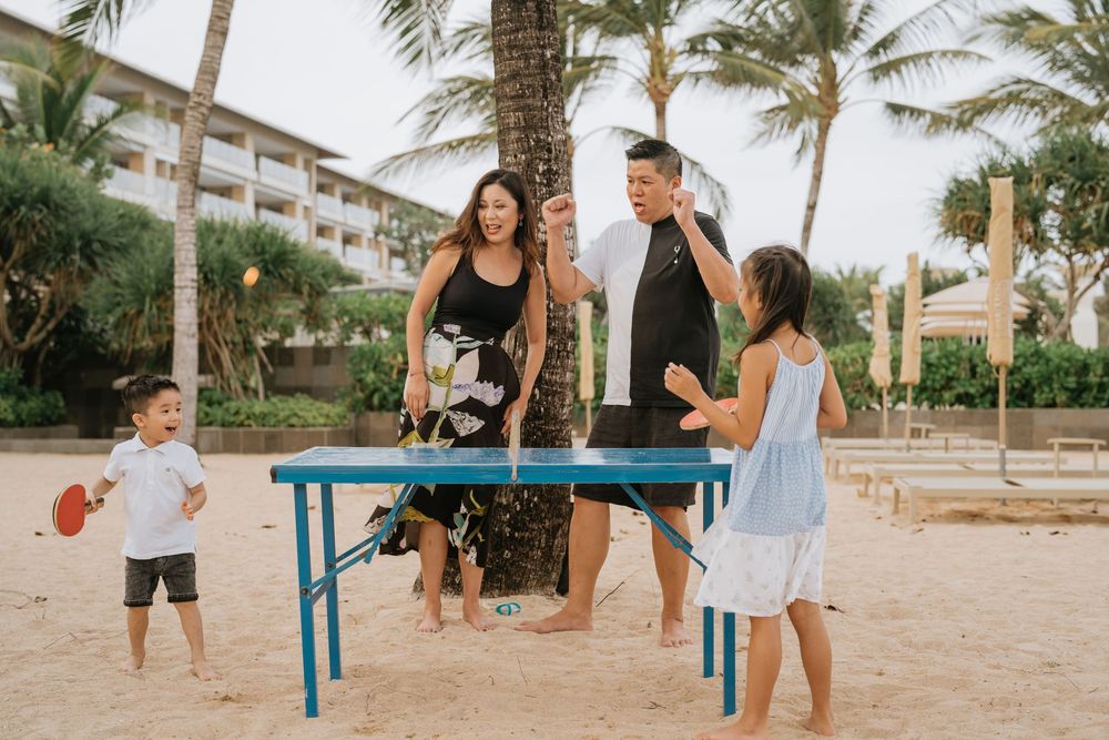 Family members engage in playful activities near a blue bench at a beachside resort.
