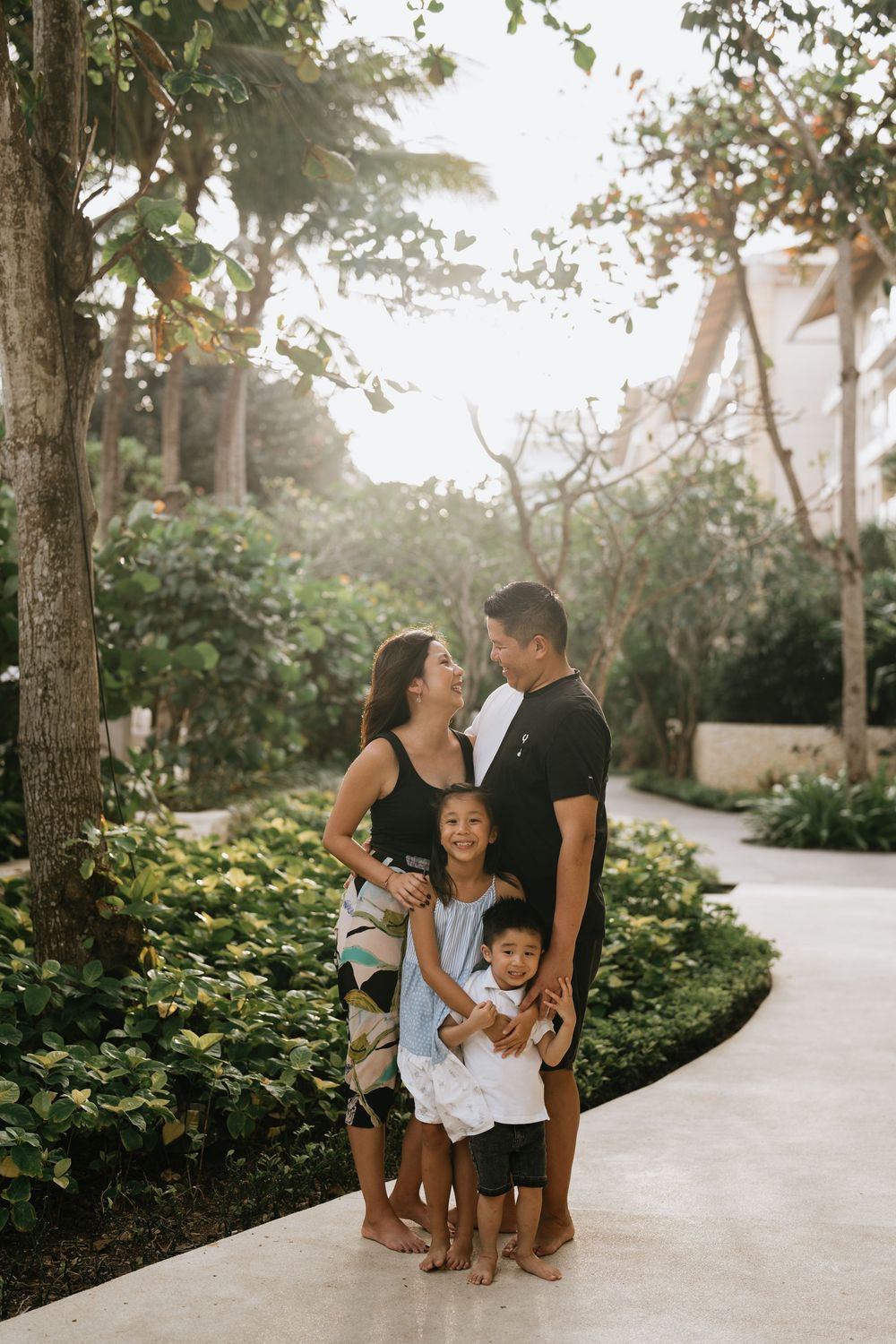 A family shares candid moments together on a palm-lined pathway at sunset.