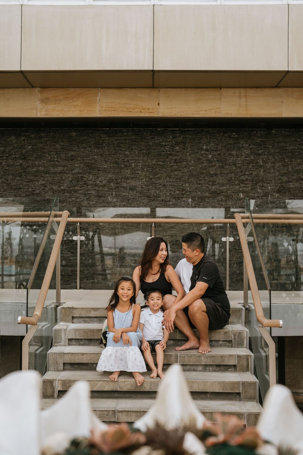 Family sits together on concrete steps at a modern tropical resort.