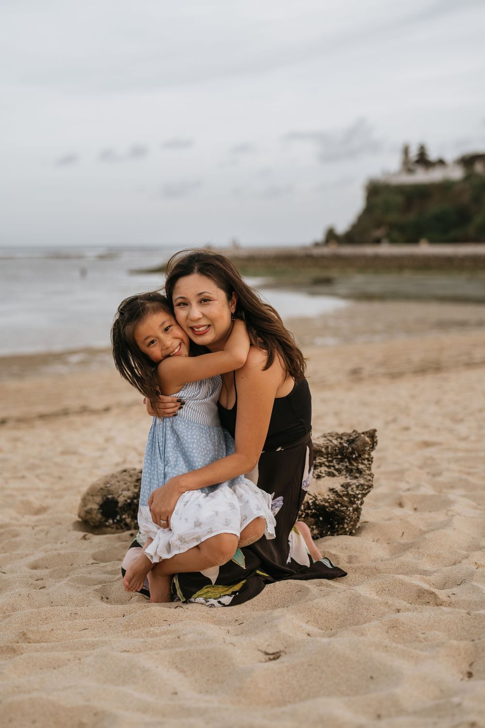 Mother and child sharing tender moments while sitting on sandy beach.