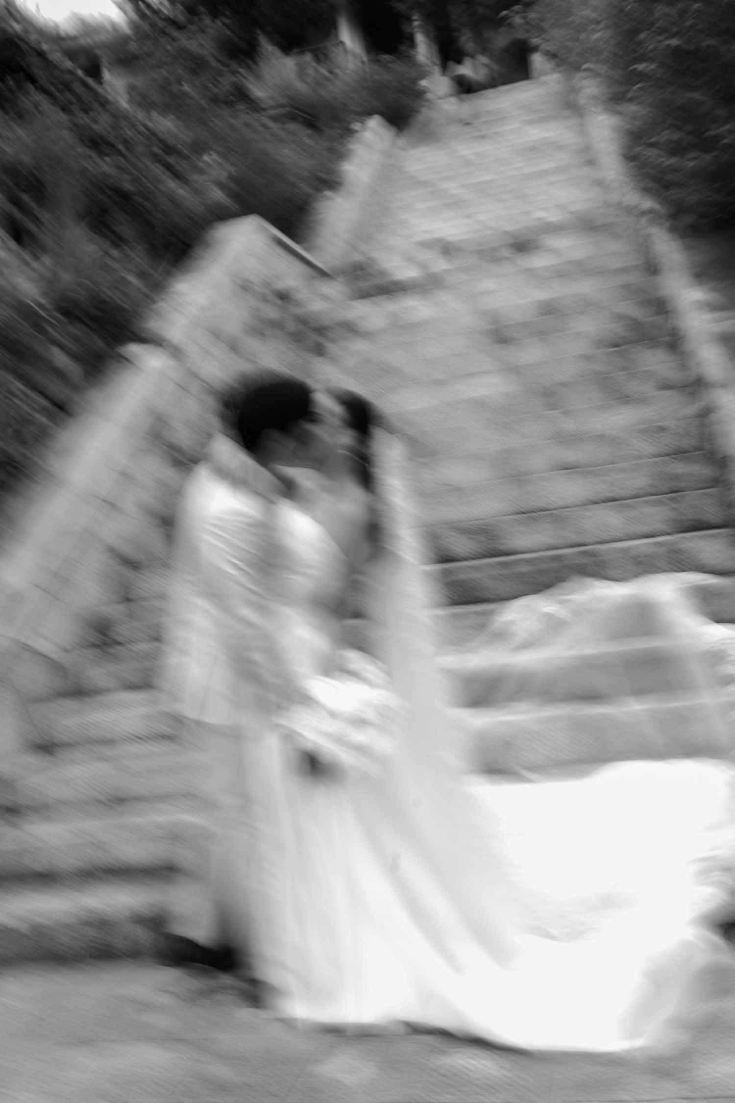 Artistic blurred black and white photo of bride and groom kissing on outdoor stone staircase.