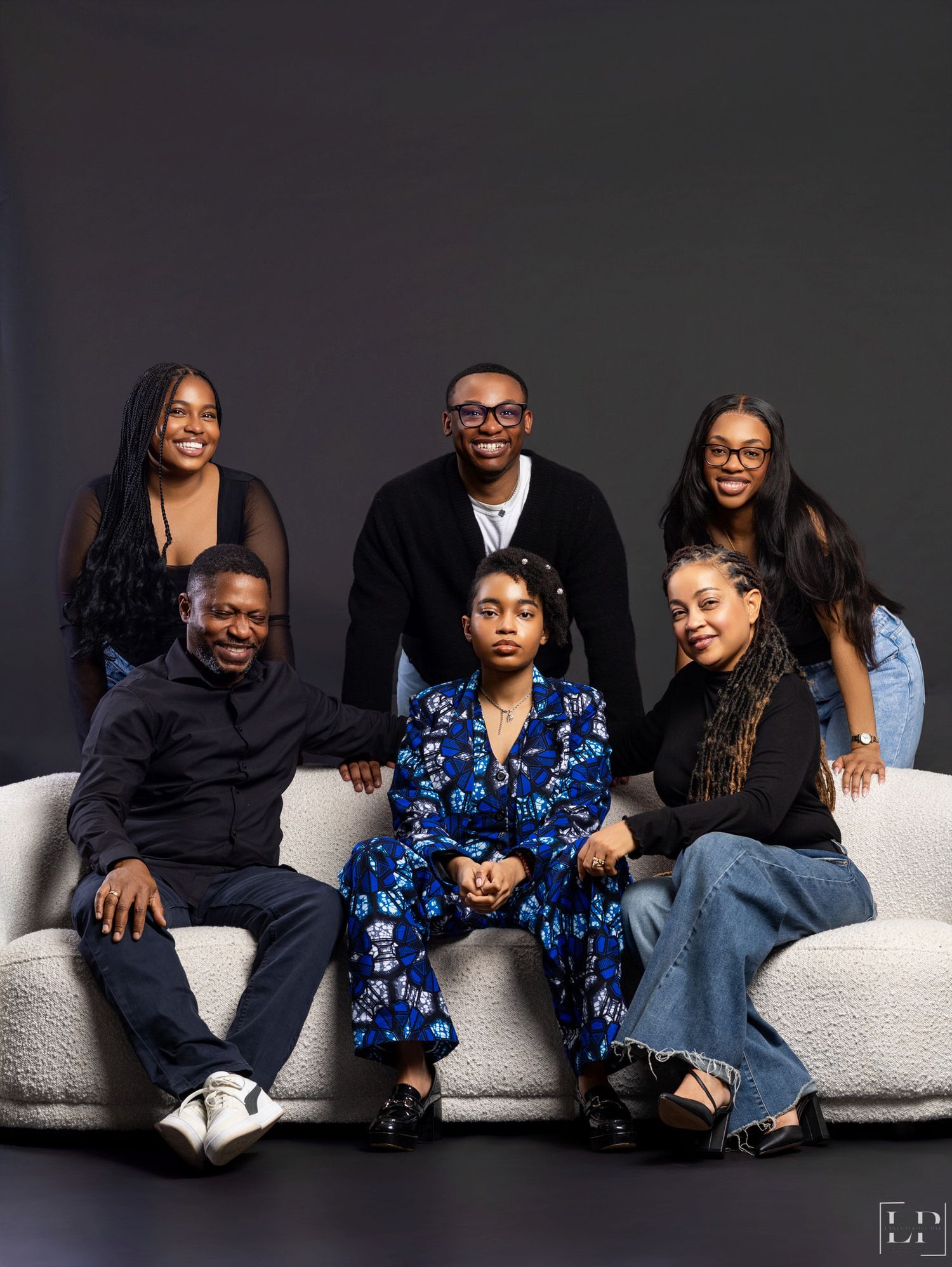 Family portrait series on white couch showing casual poses in coordinated blue and black outfits.