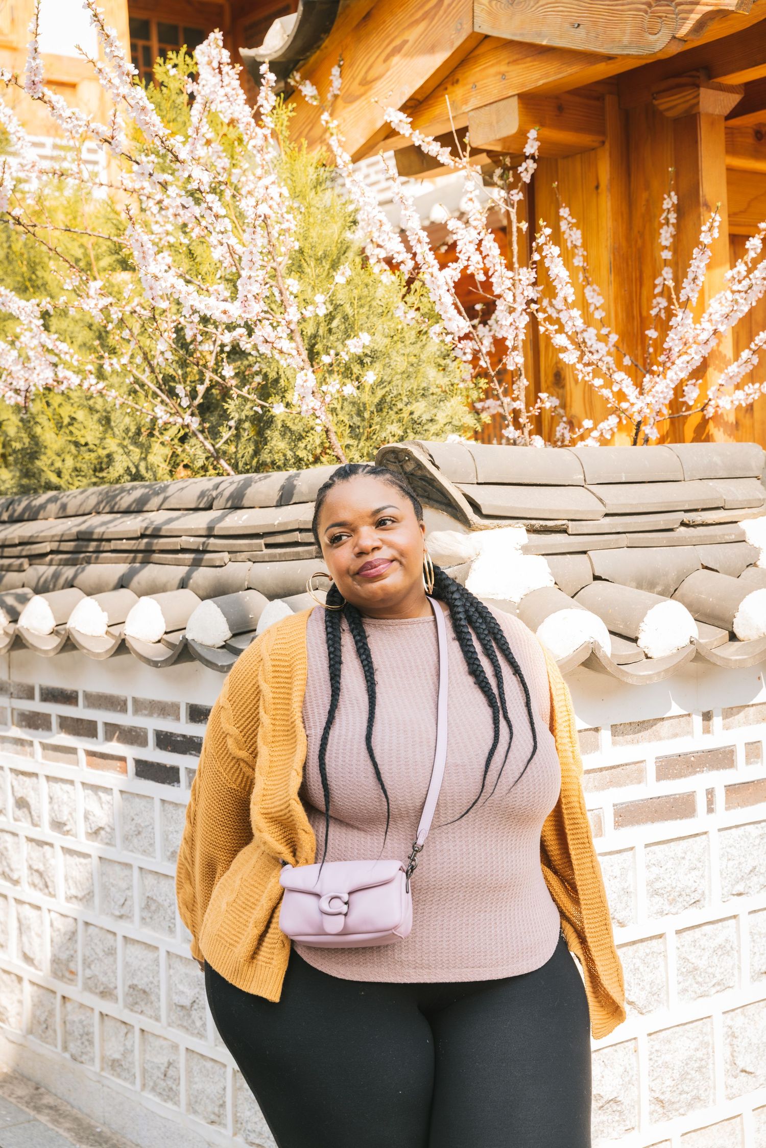 A series of fashion photos showing a beige sweater styled with a mustard cardigan and dark pants against a stone wall backdrop.