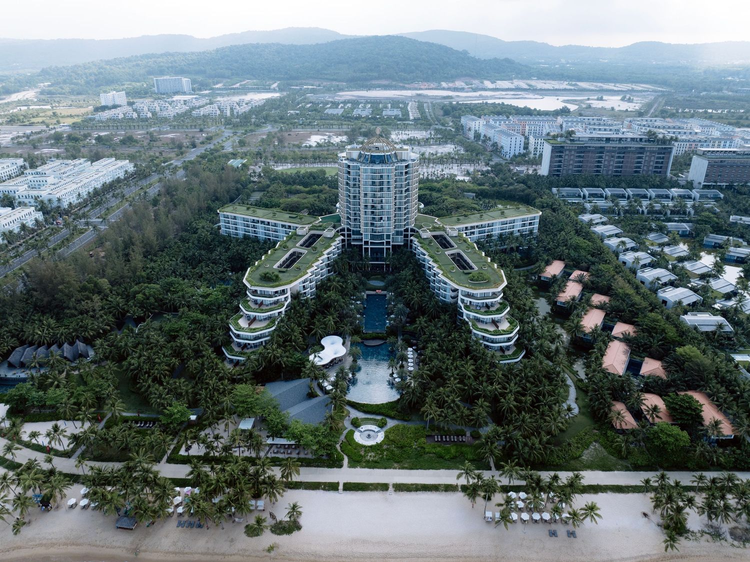 Aerial view of a luxury tropical beachfront resort surrounded by lush palm trees and manicured gardens.