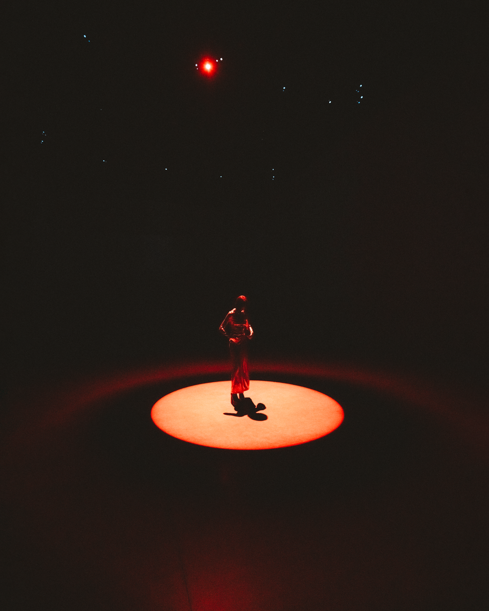 A performer in a red spotlight dances on stage creating dramatic silhouettes against a dark background.