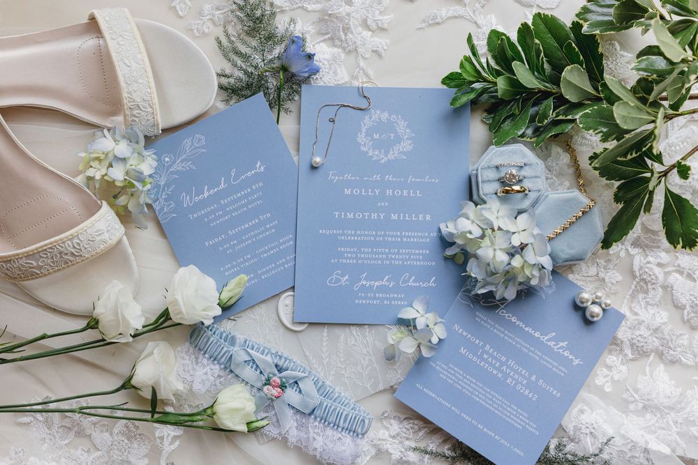 Light blue wedding invitations styled with delicate white flowers and greenery on white lace fabric.Newport, RI Wedding photography