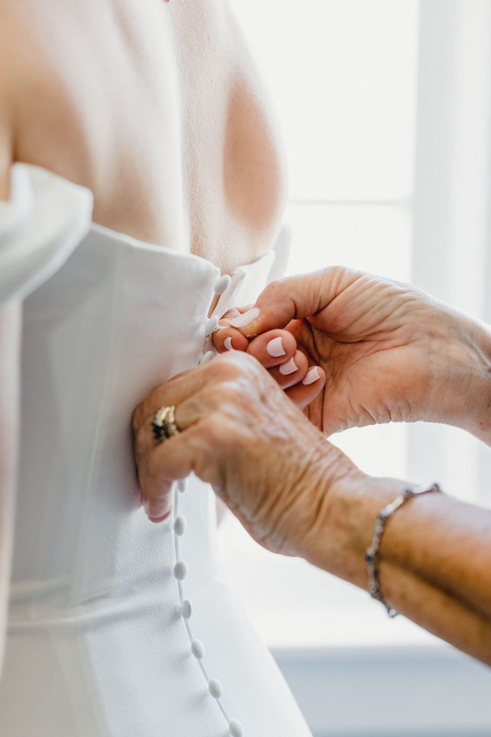 Close-up view of hands fastening buttons on a white wedding dress in natural light.Newport, RI Wedding photography