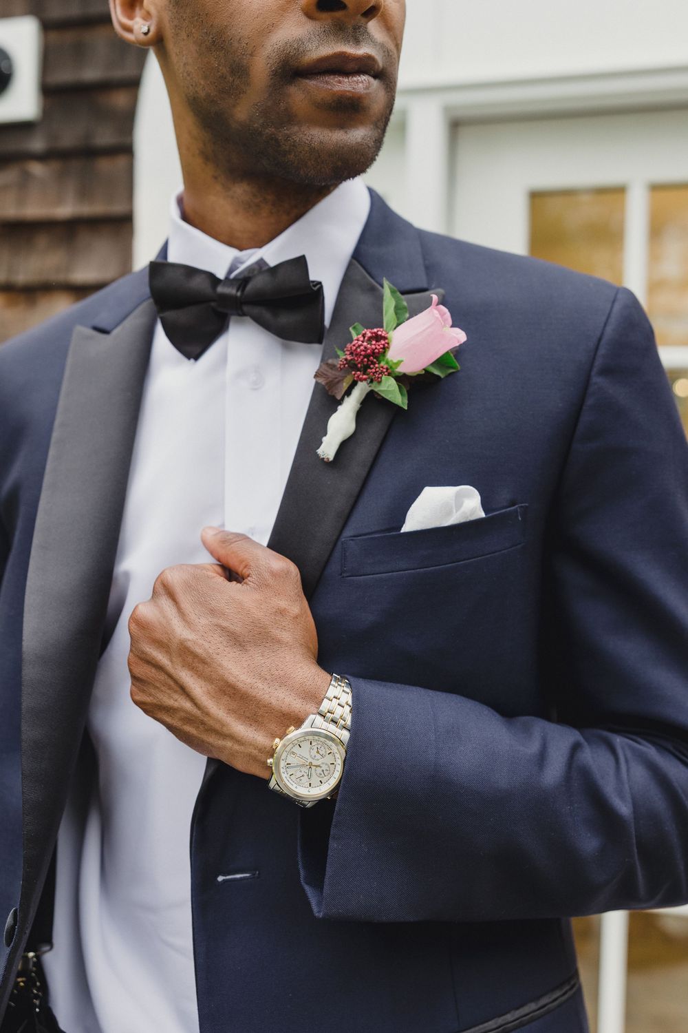 Close-up view of a groom in navy tuxedo with pink boutonniere and white dress shirt adjusts his formal attire.
