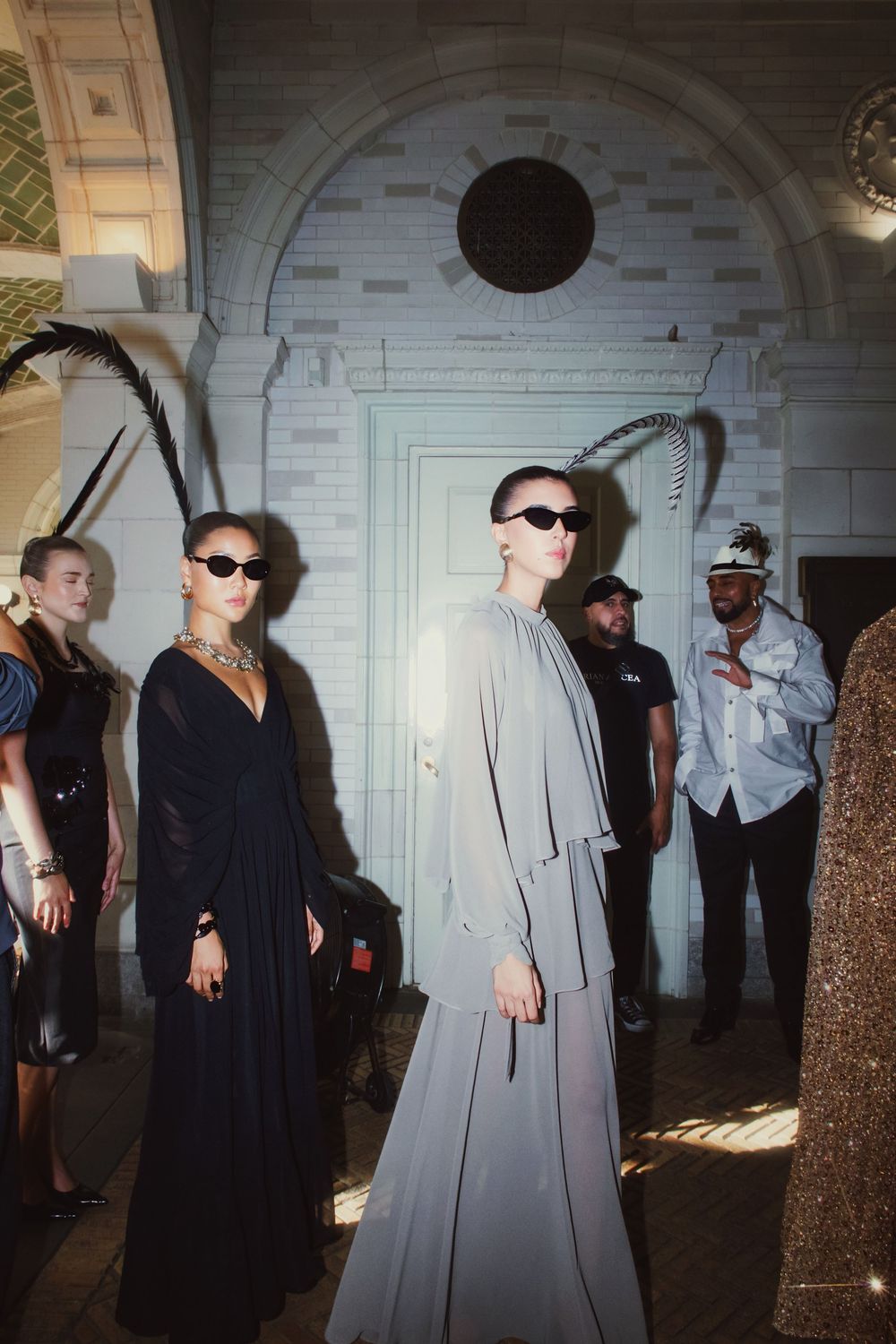 Group of people in formal attire standing in an ornate hallway with white architectural details and arched doorways.