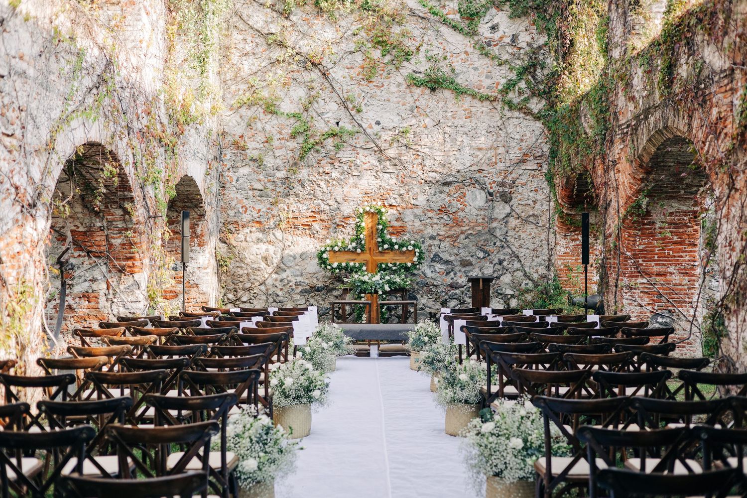 Outdoor wedding ceremony setup with rows of black chairs and natural stone wall backdrop.