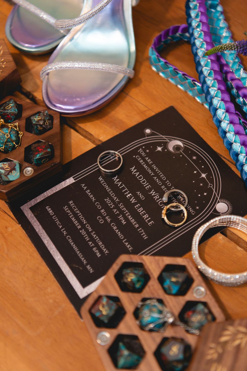 Black celestial-themed wedding invitations displayed next to turquoise dice and decorative elements on a wooden surface.