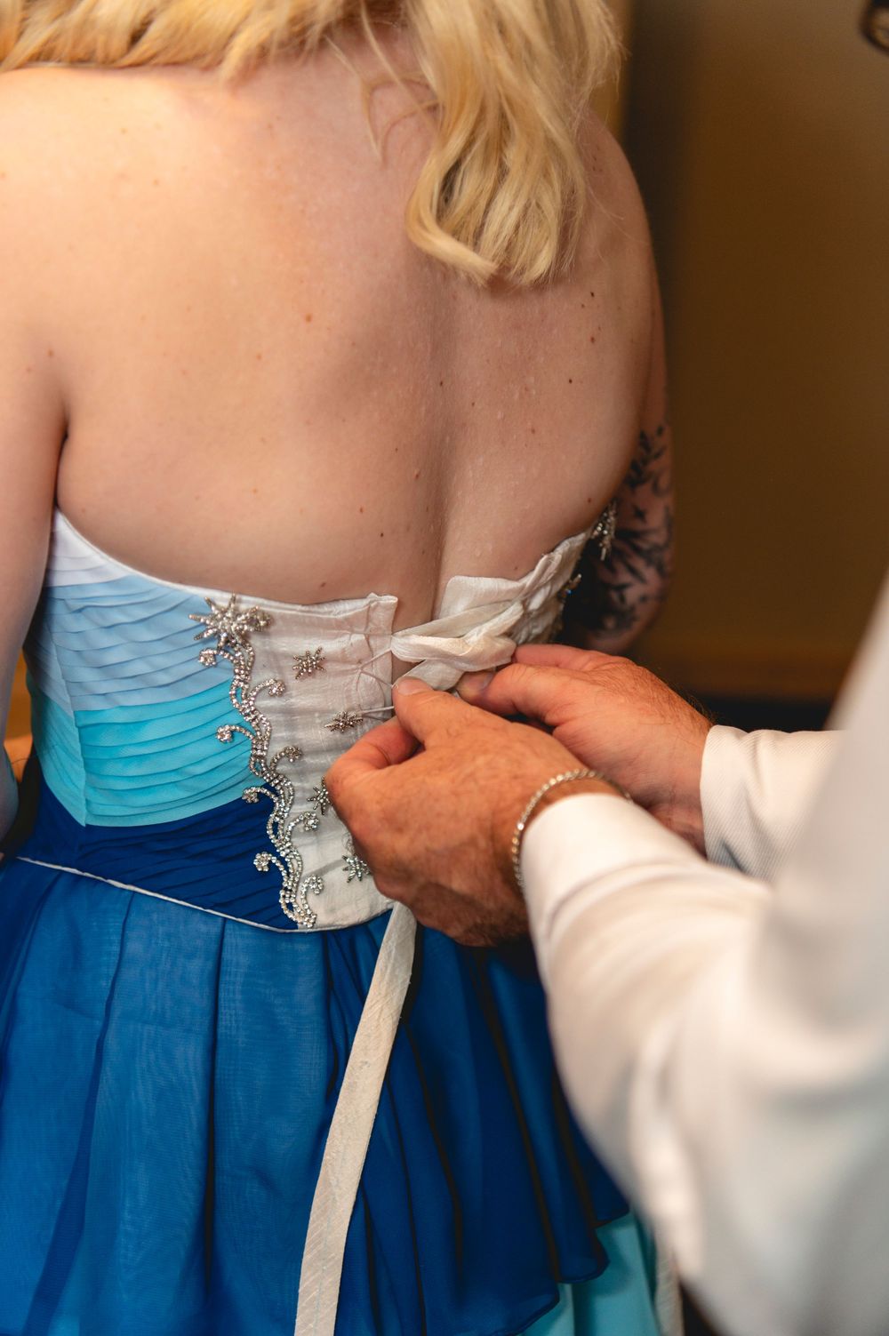 Hands lacing up the back of a turquoise and white dress showing a wedding dress preparation detail.