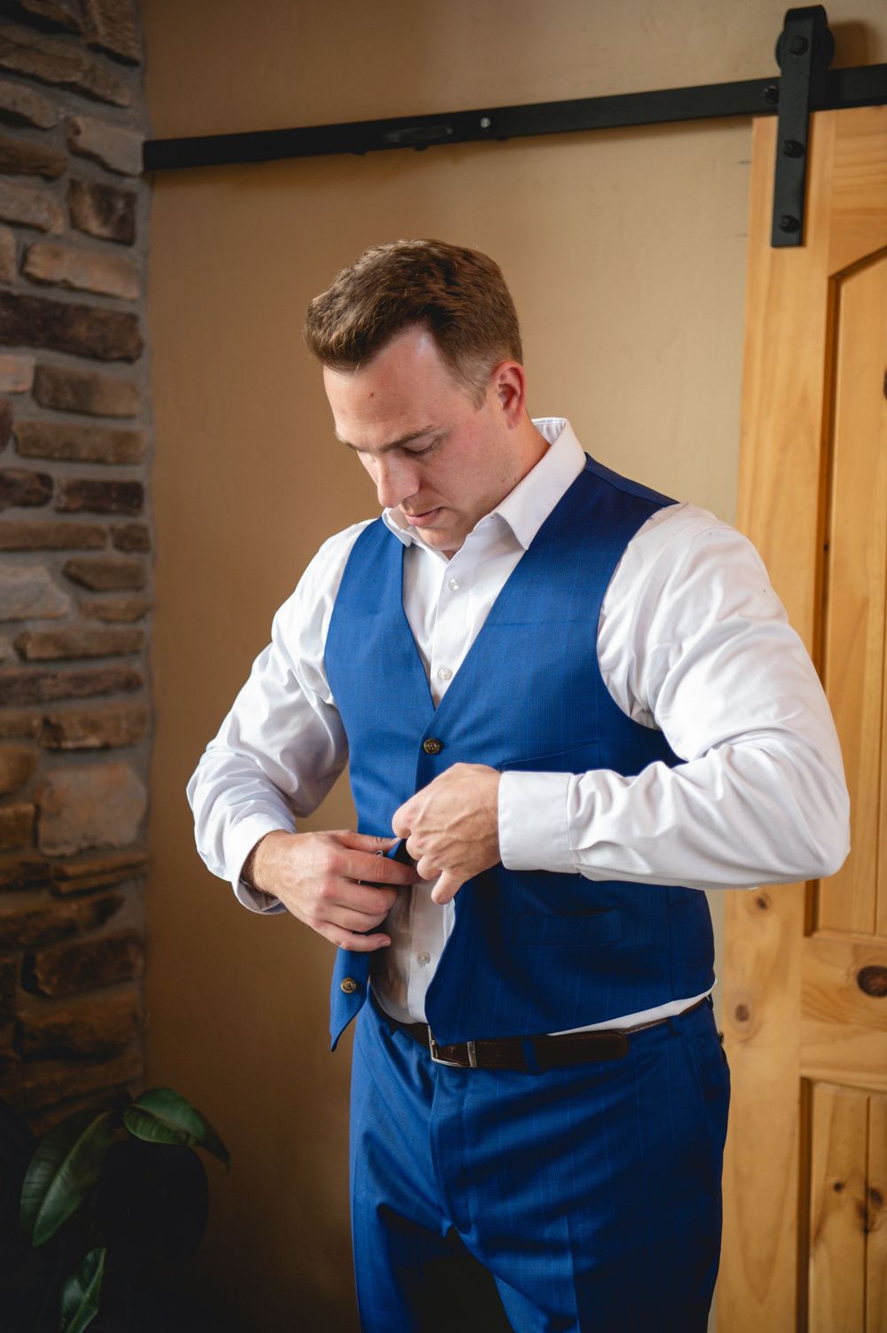 Someone getting dressed in formal attire adjusts their bright blue vest over a crisp white dress shirt.