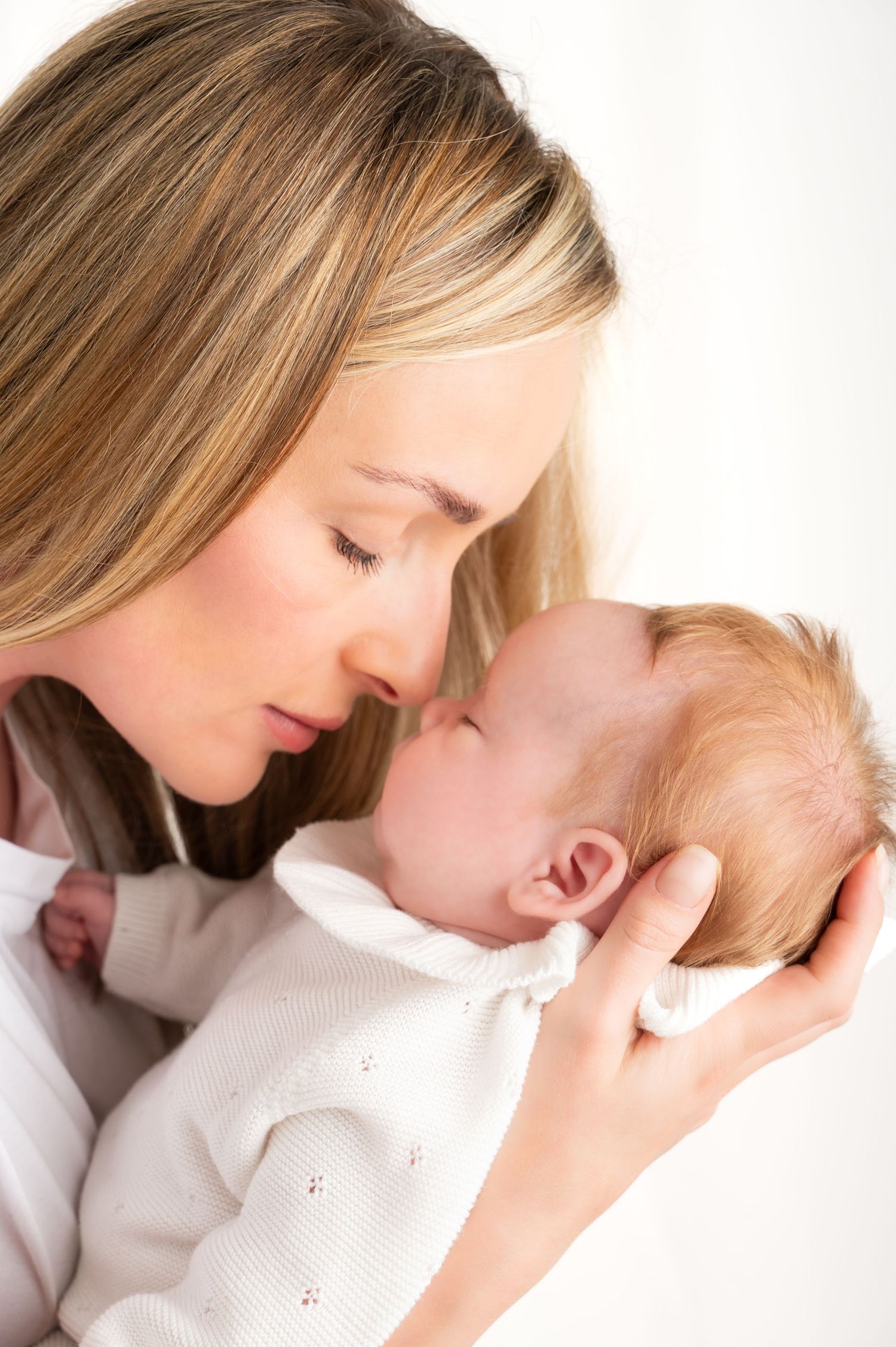 Tender series of a mother cuddling with a baby in white against light background, Carluke Studio.