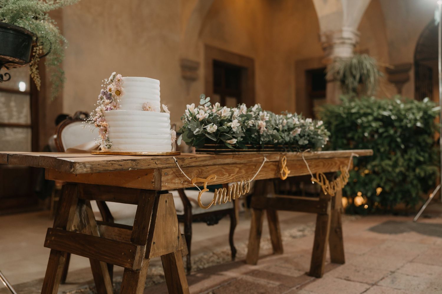 Wedding cake display with greenery and rustic wooden elements in an elegant venue setting.