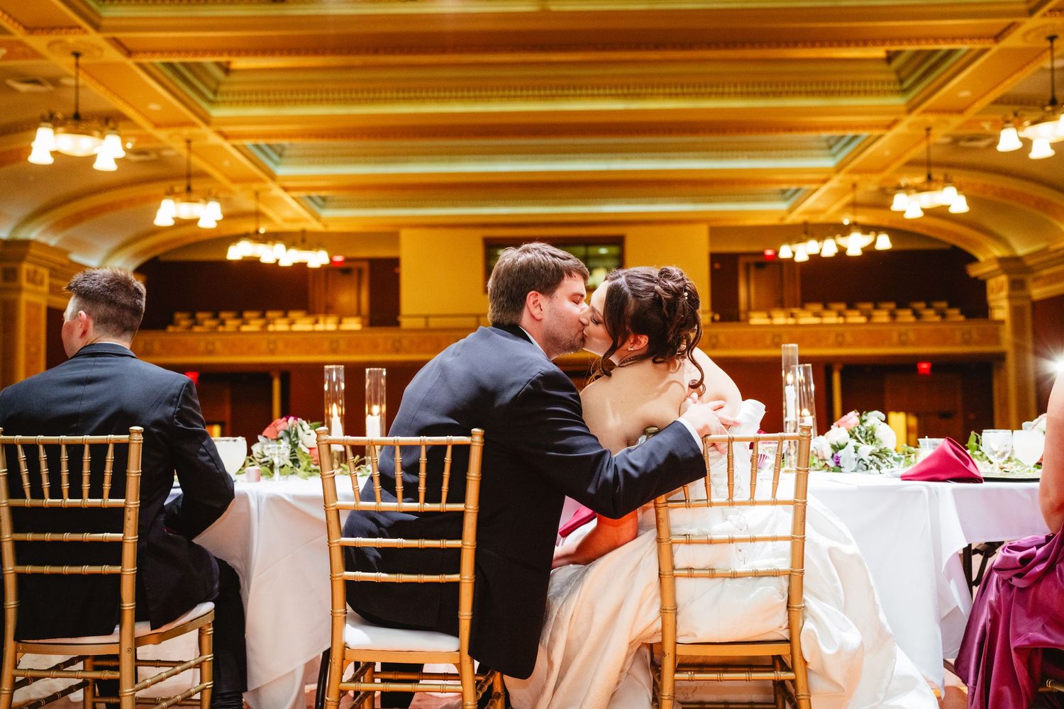 People dancing at an elegant indoor wedding reception in a warmly-lit ballroom with golden decor.
