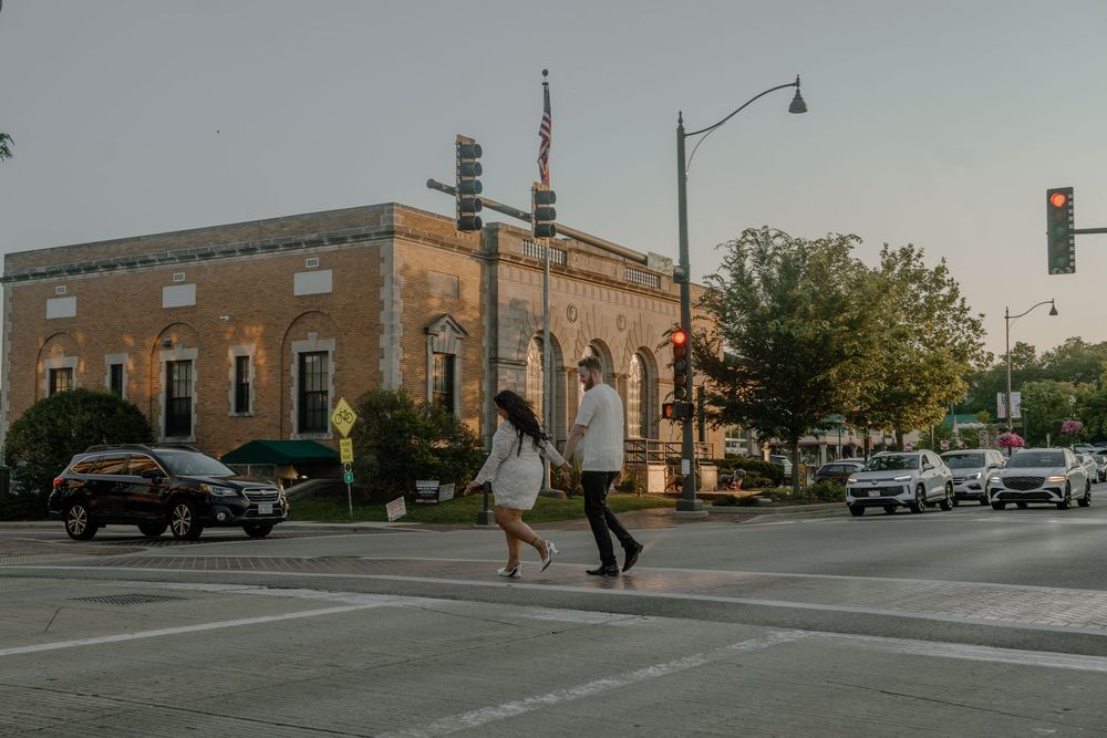Historic brick buildings line the small-town intersection with parked cars along the street on a cloudy day.