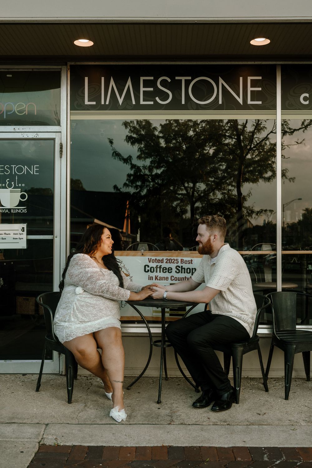A couple sitting at an outdoor coffee shop patio share a playful moment across a table at Limestone Coffee.