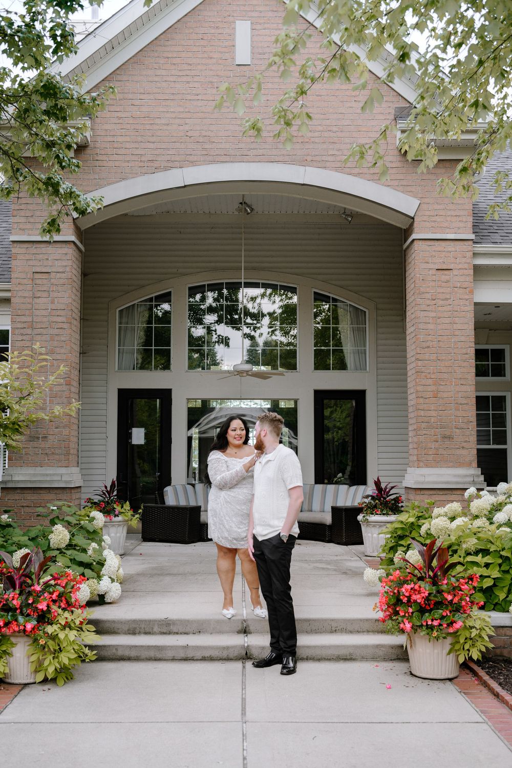 A romantic couple shares a tender moment in front of a brick and stone church entrance with blooming flower planters.
