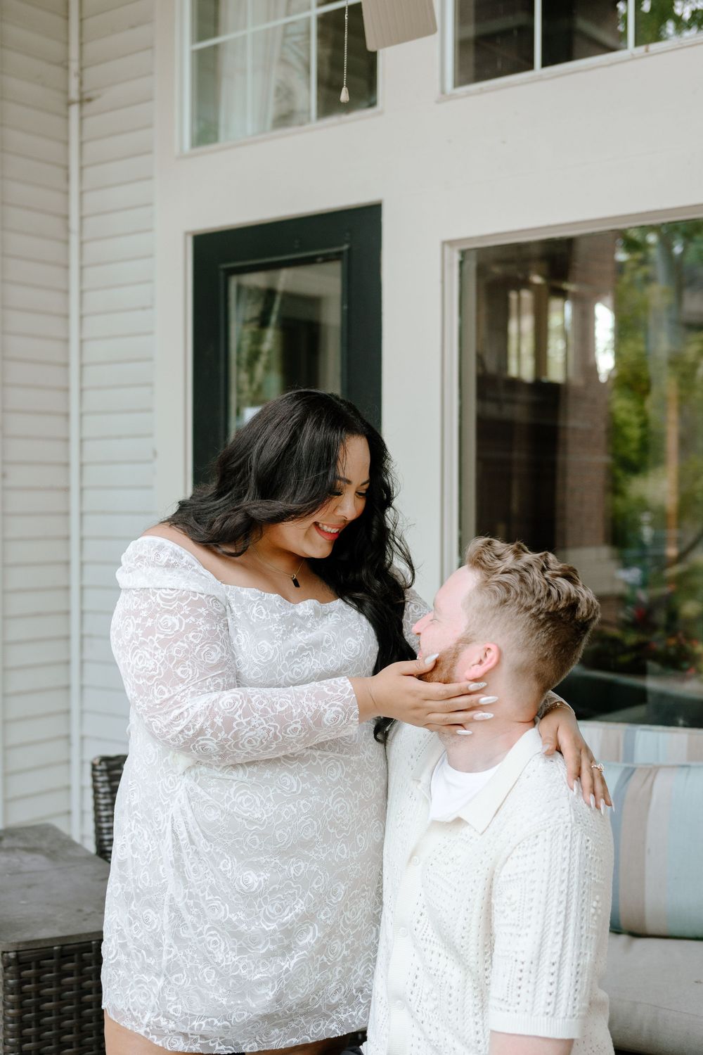 A romantic couple in matching white lace outfits sharing an intimate moment on a front porch.