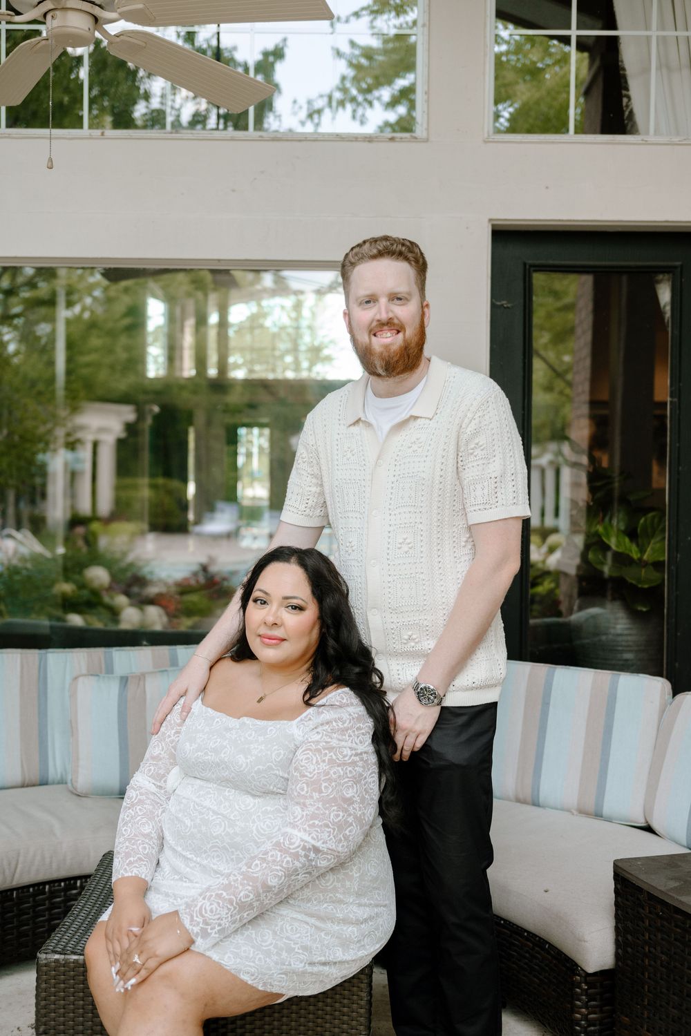 A wedding couple poses together on an elegant patio with glass walls and blue striped furniture.