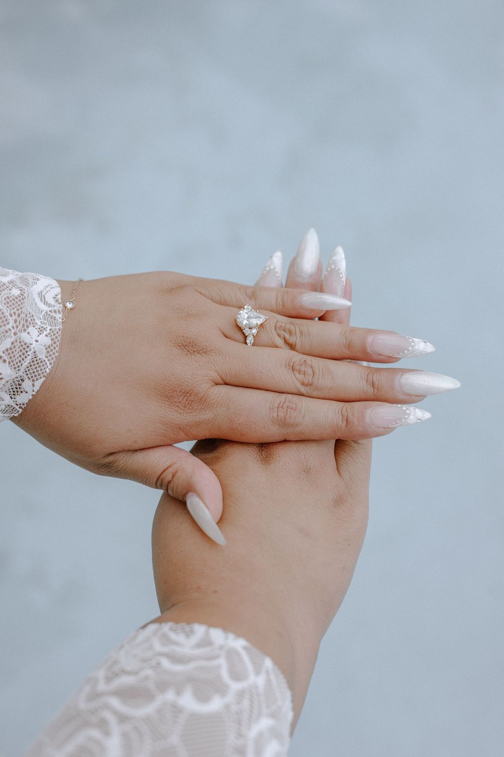 Close-up of hands wearing delicate white lace sleeves and long acrylic nails with engagement ring.