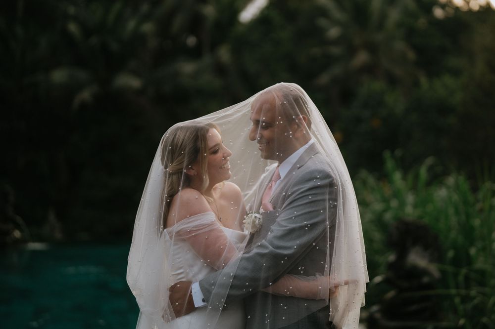 A couple shares romantic moments under a flowing white veil in an outdoor setting.
