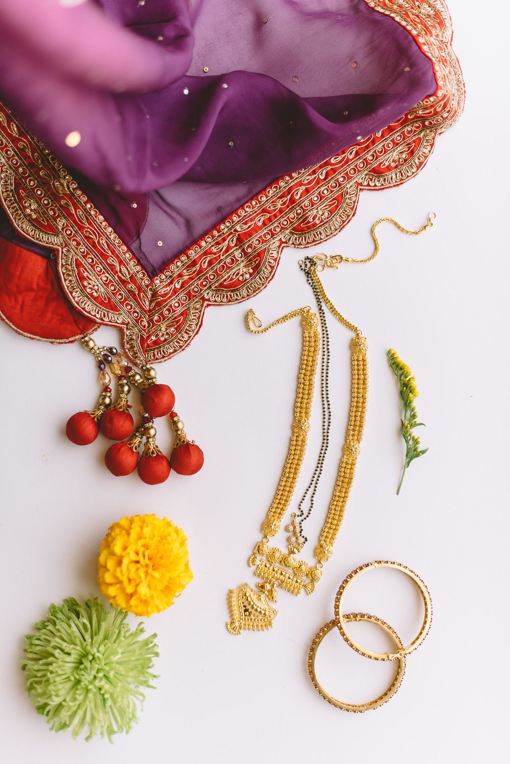 Colorful traditional Indian jewelry set featuring earrings with marigold and red pom pom accents against a purple fabric.