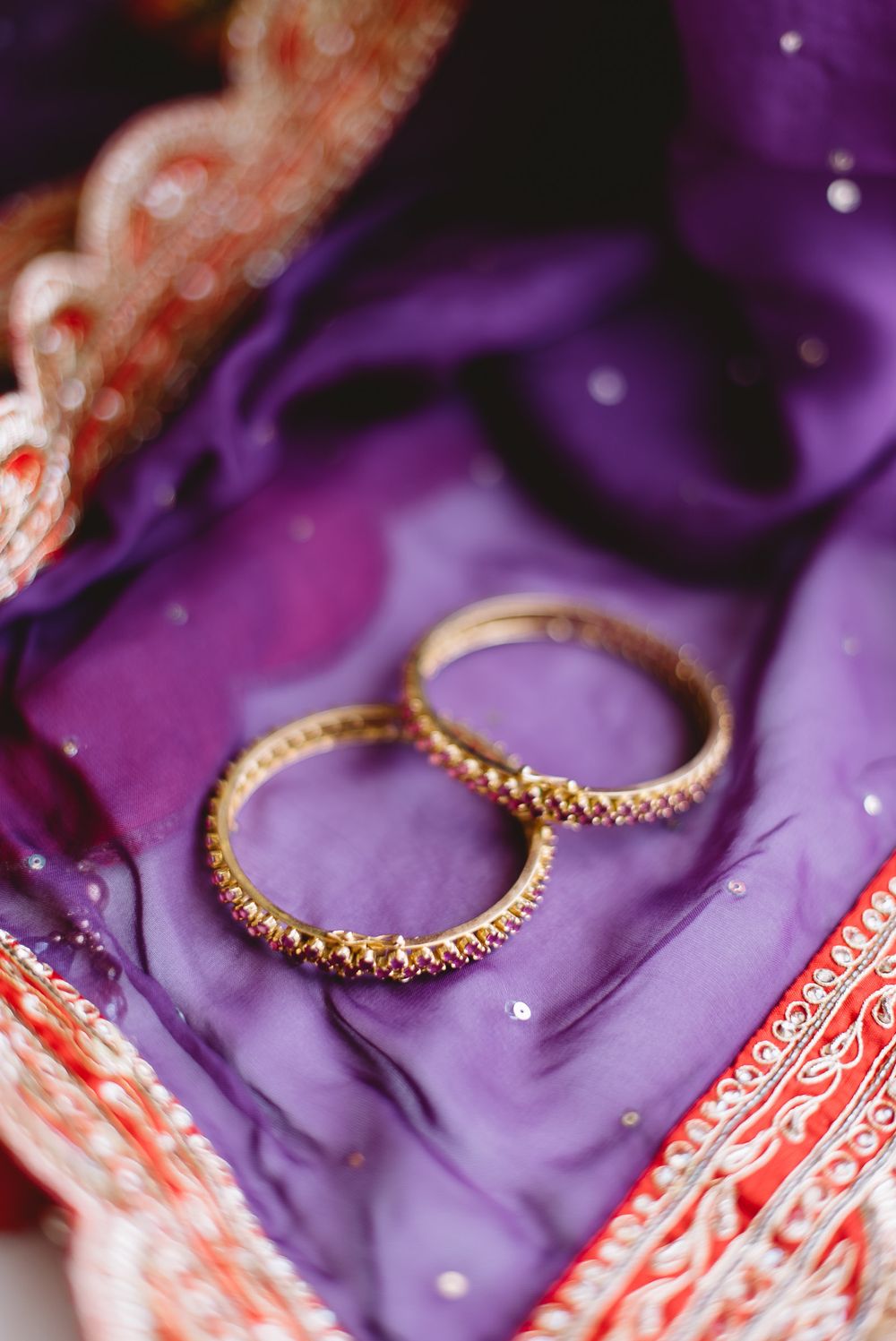 Gold wedding rings displayed on vibrant purple satin fabric with red and pink decorative accents.
