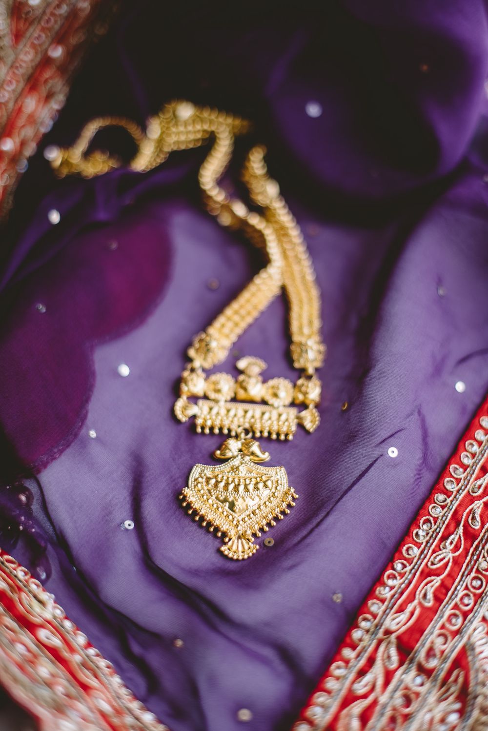 Gold traditional Indian mangalsutra necklace with pendant photographed against purple fabric background with sparkles.
