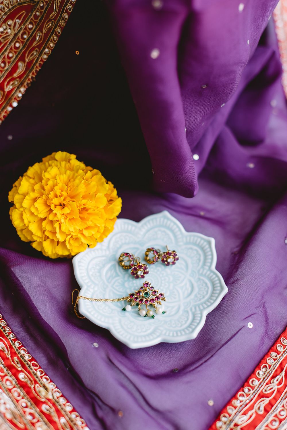 Small gold marigold flower rests on a white lace doily against a purple silk background in elegant jewelry display.