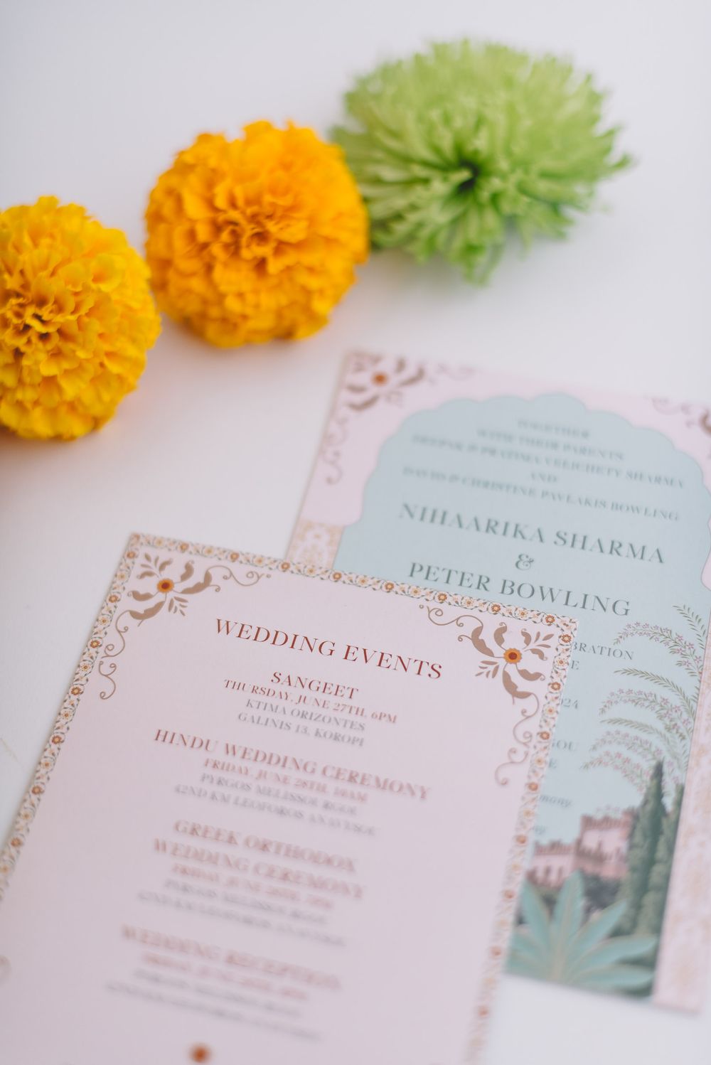 Wedding invitation cards with orange marigolds and green chrysanthemum flowers on a white surface.