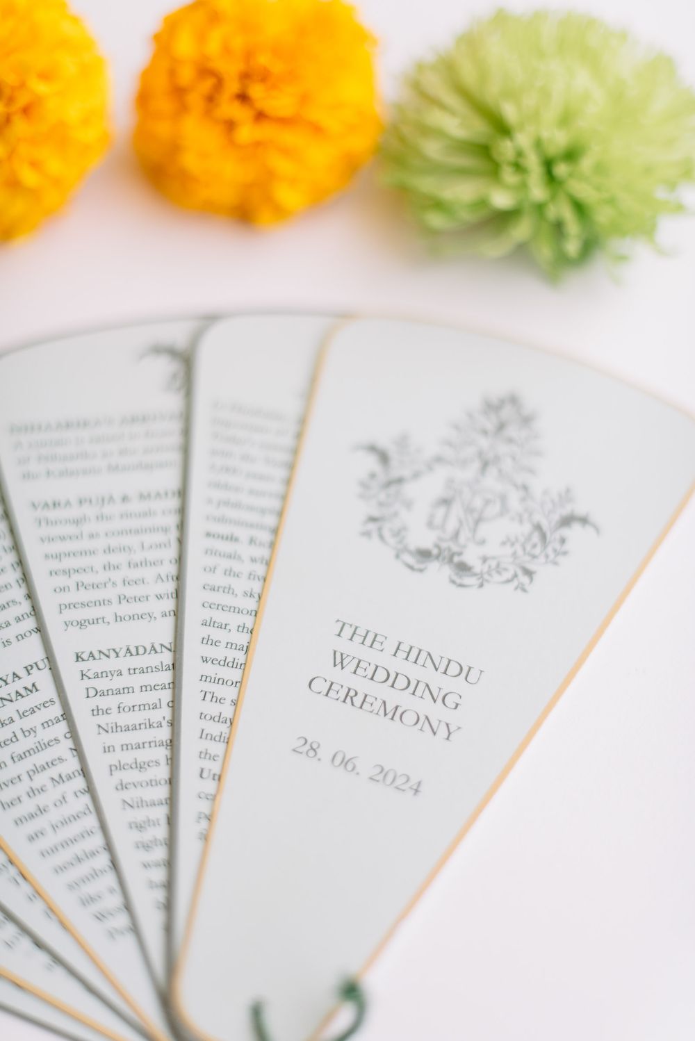 Close-up of traditional Hindu wedding ceremony program booklets with ornate designs and orange flowers.