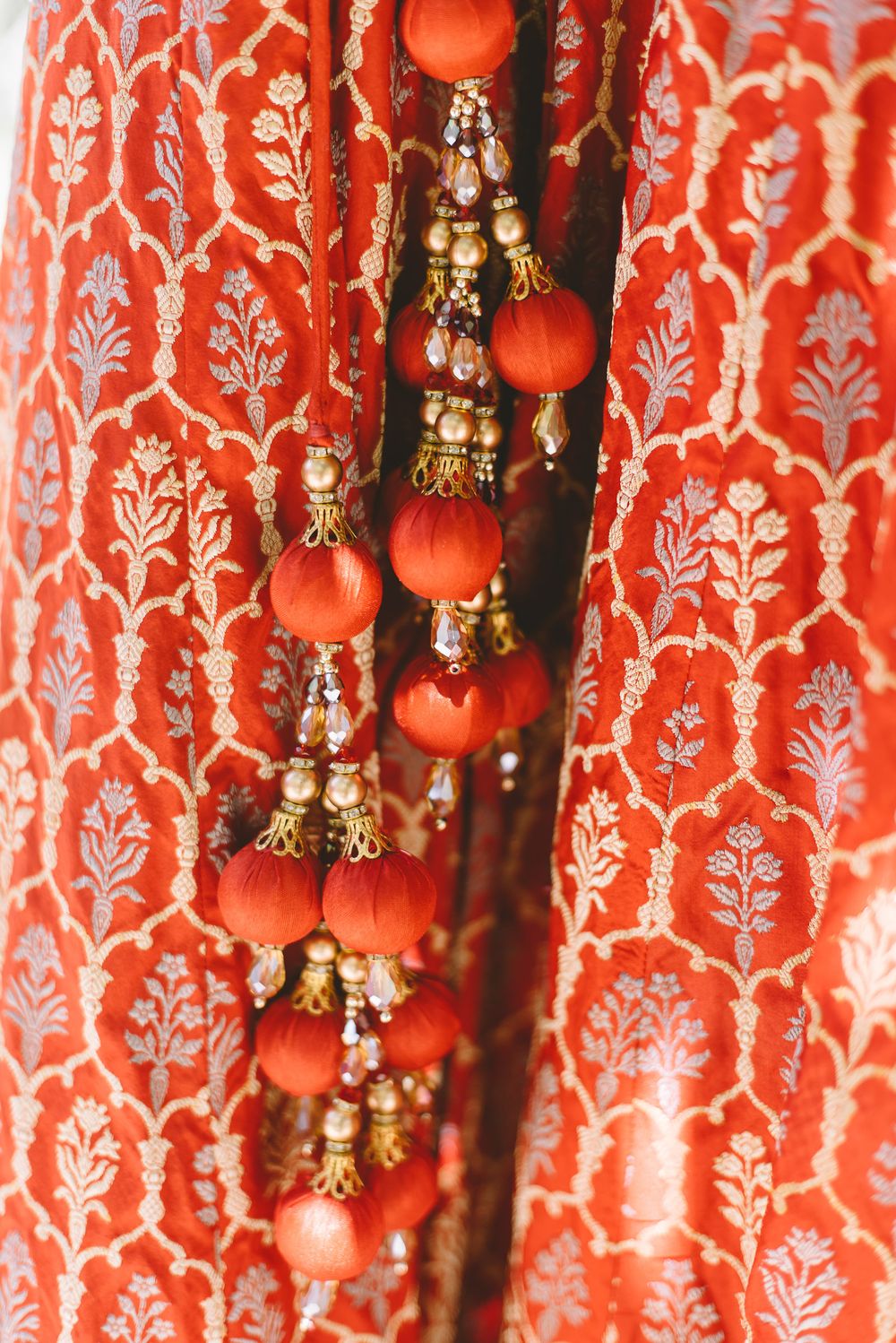 Red floral curtains or drapes with traditional Indian decorative bells and tassels hanging against a patterned background.