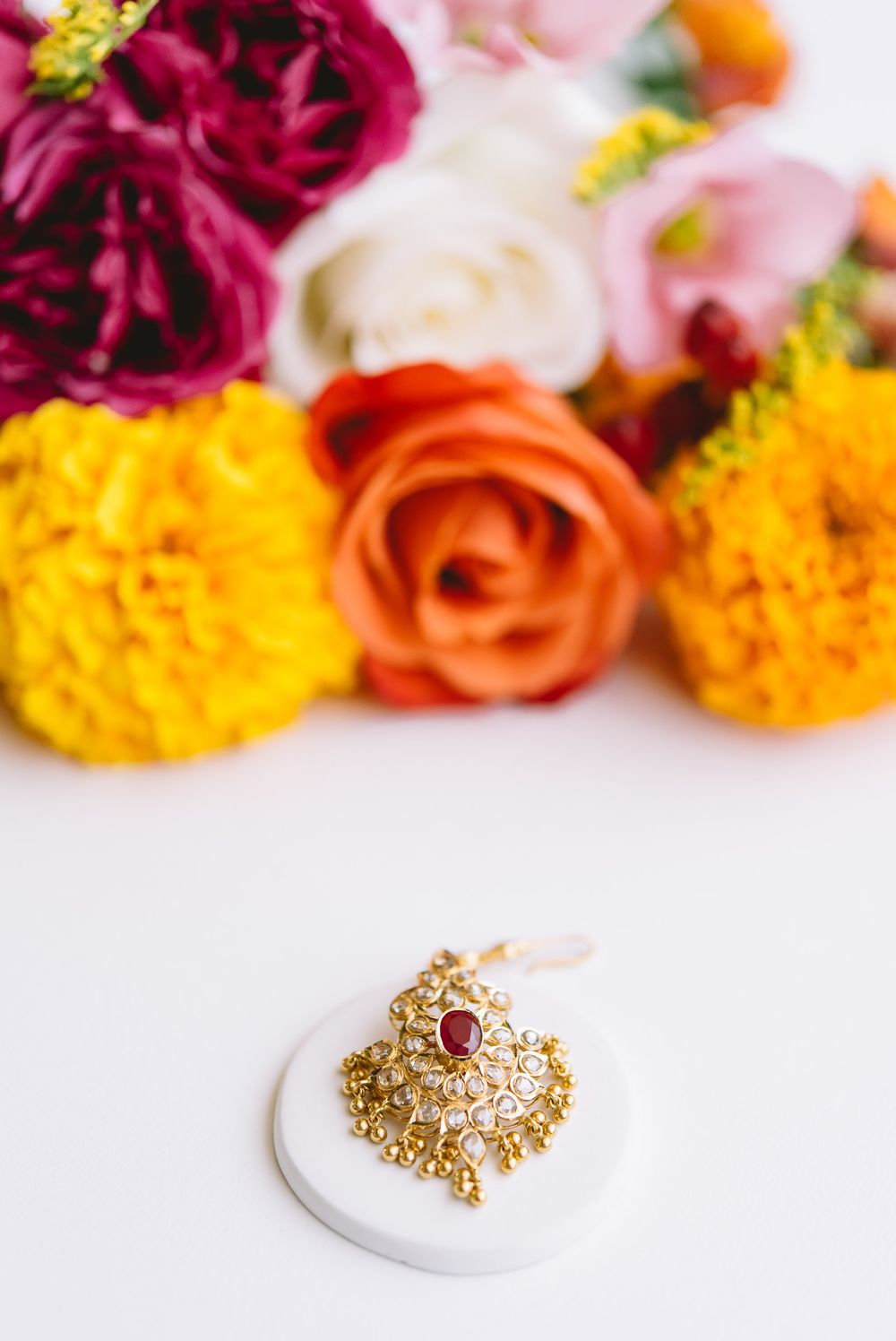Luxurious gold and ruby ring displayed with vibrant pink and orange florals against a white backdrop.
