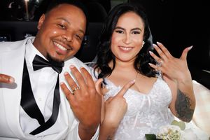 Wedding couple in white attire poses together showing off their rings at a formal celebration.