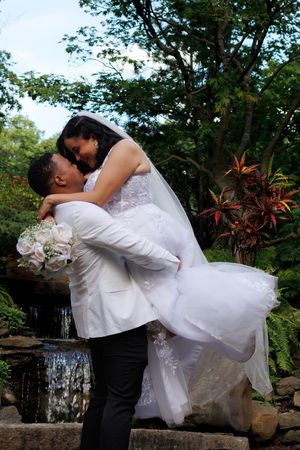 Romantic wedding couple embraces by a cascading waterfall and garden pool with tropical foliage.