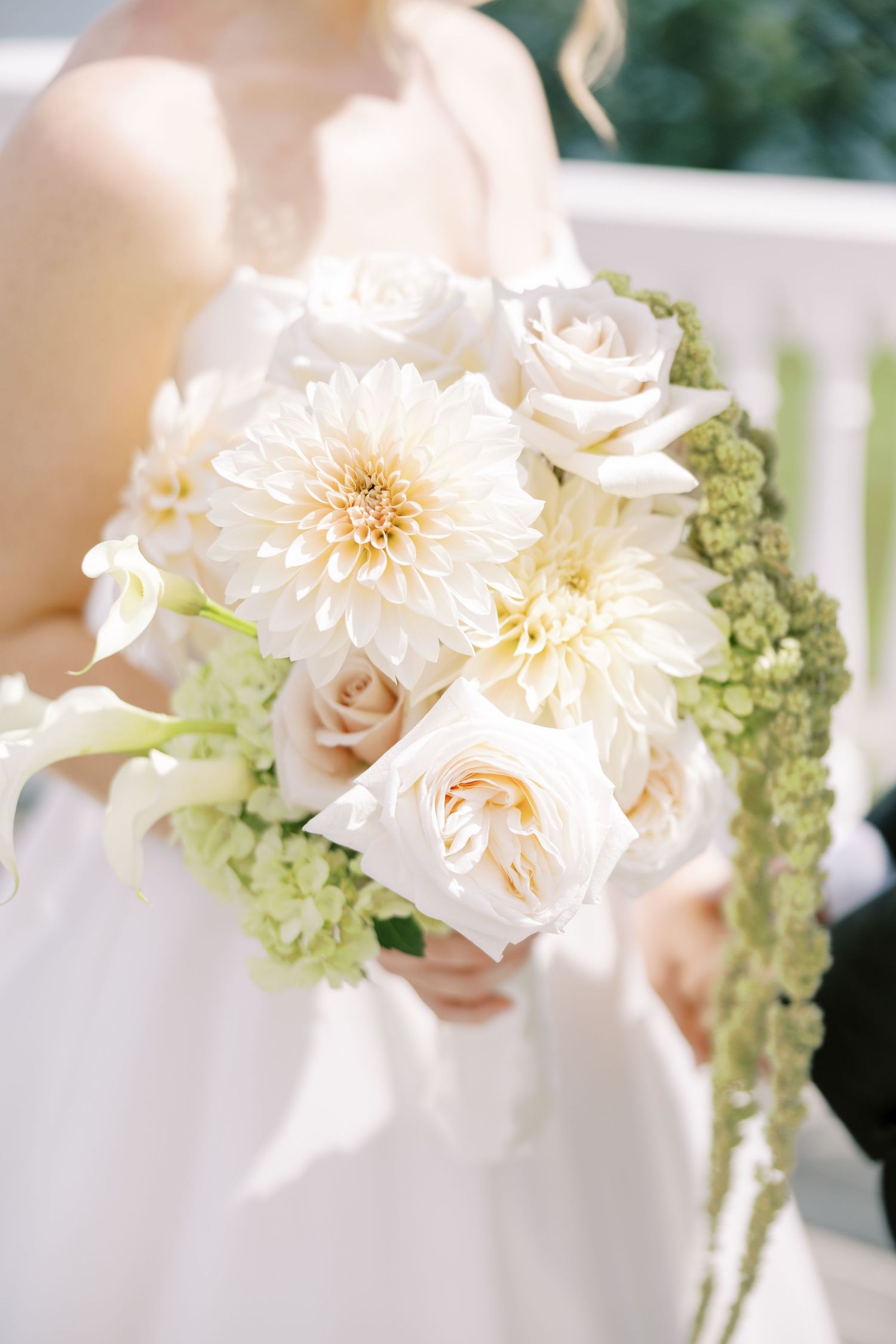 Close-up view of an elegant bridal bouquet with white dahlias, roses and pale green hydrangeas against a light background.