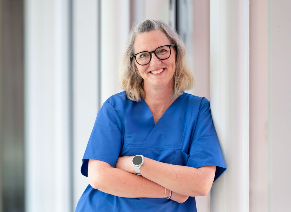 Healthcare professional in blue scrubs smiling against white column background.