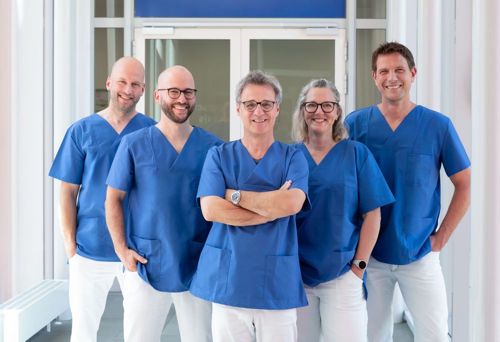 Healthcare team wearing blue uniforms standing together in modern medical facility corridor.