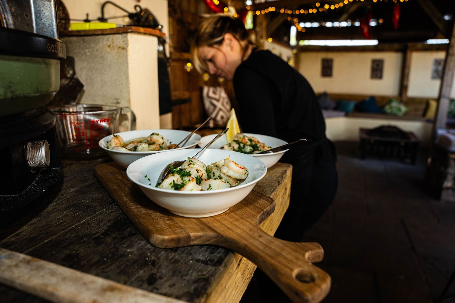 a chef cooks at a party with a pizza oven. 3 bowls of prawns sit on a wooden chopping board