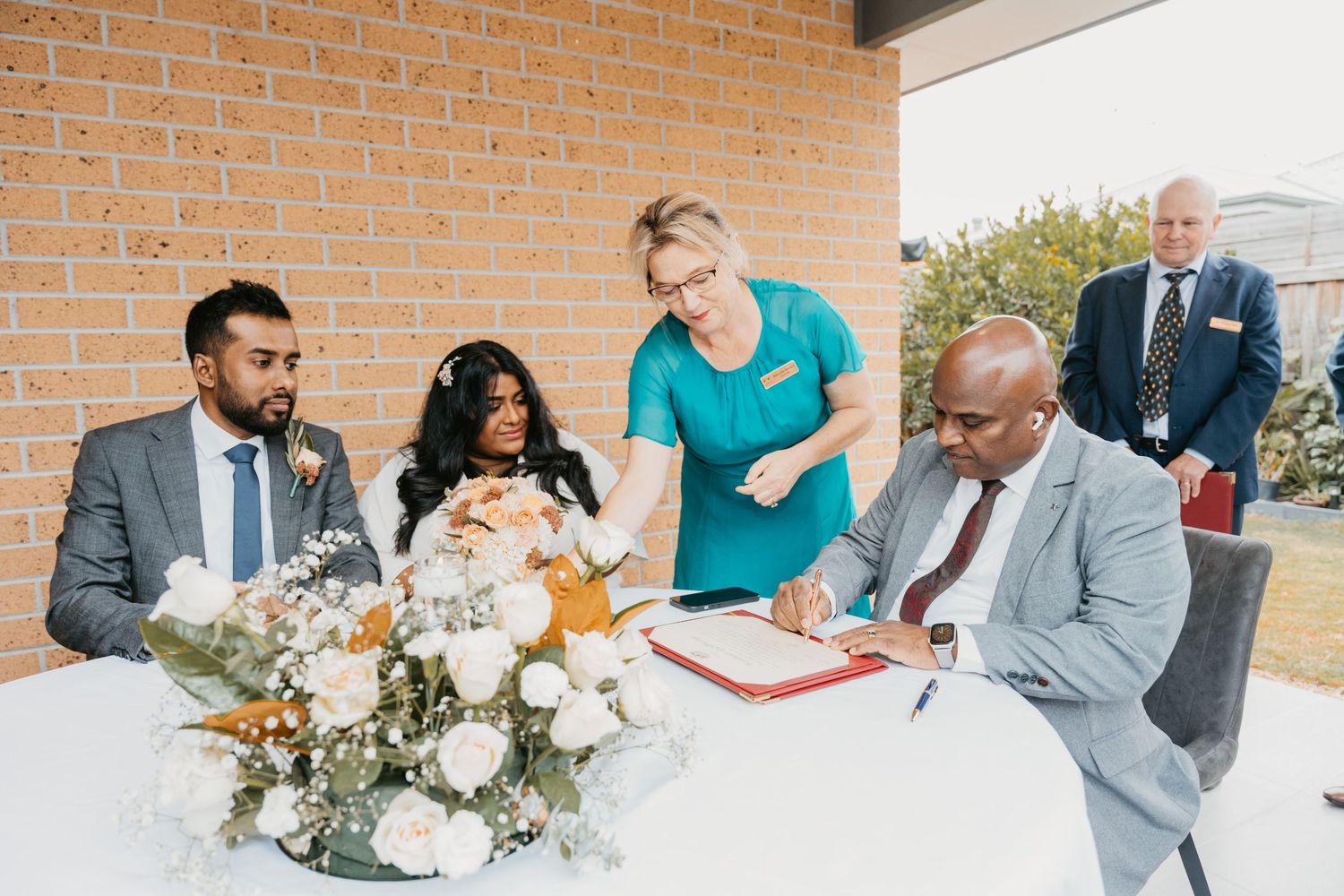 A collage of newlyweds signing marriage documents at a wedding ceremony with floral decor and witnesses present.
