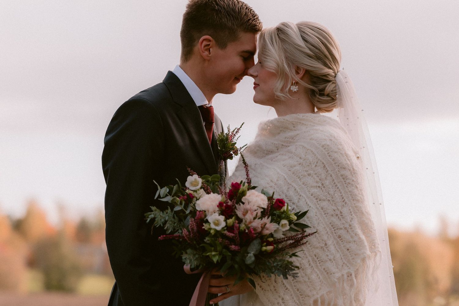 A romantic black and white photo captured through a vintage car window at a wedding.