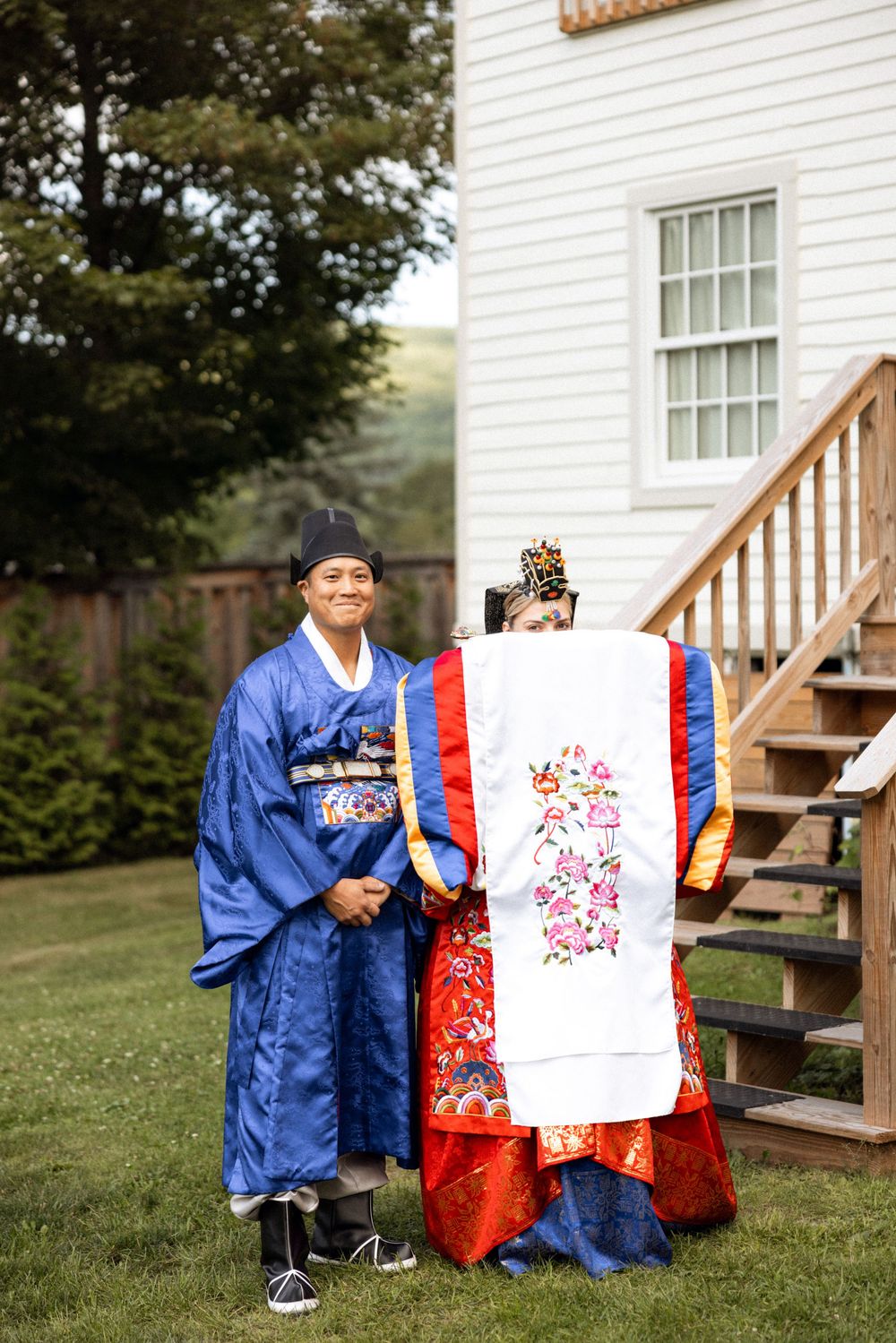 Traditional Korean wedding display with blue and red hanbok outfits against white building backdrop.