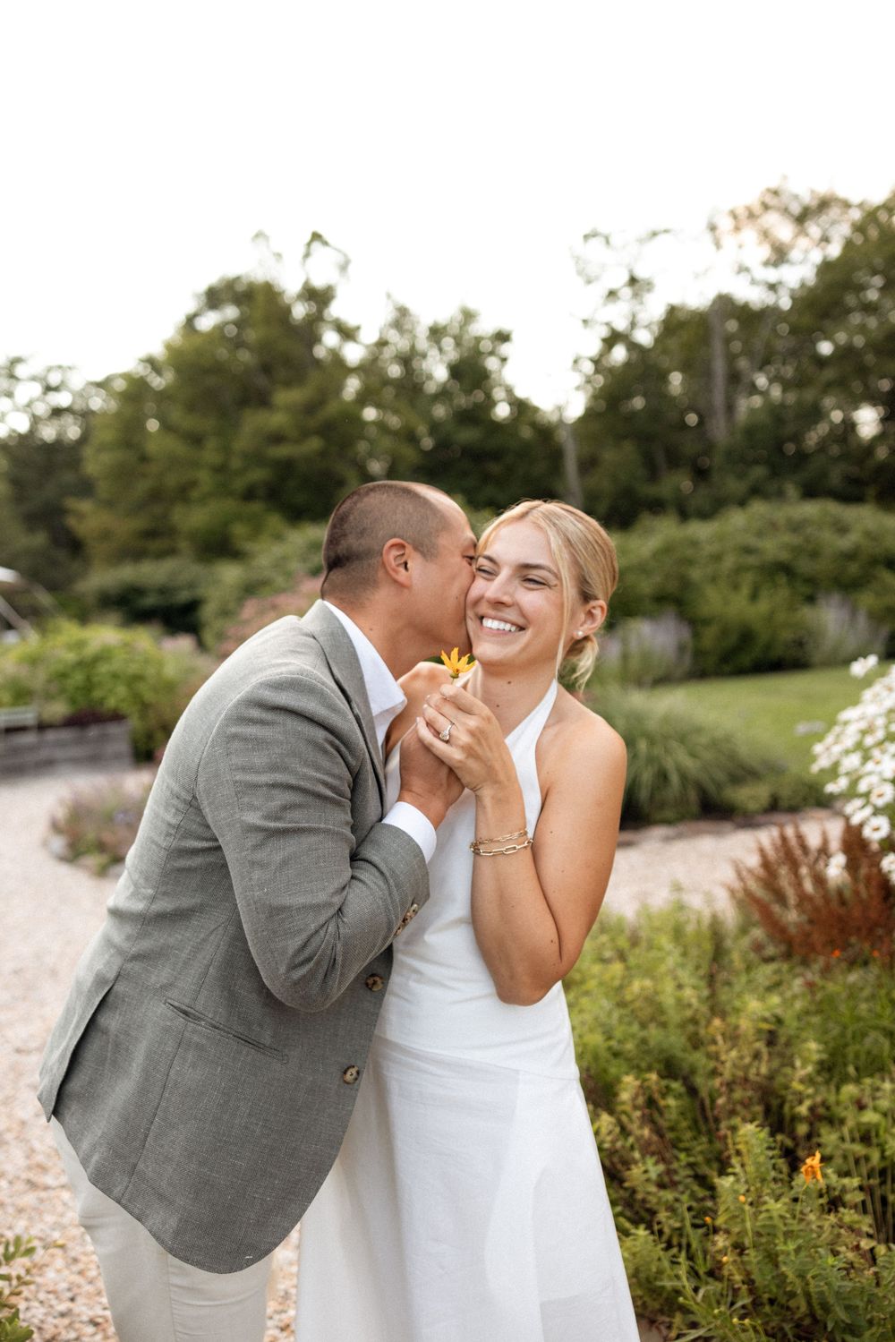 Candid moment of laughter between newlyweds in a blooming garden pathway.