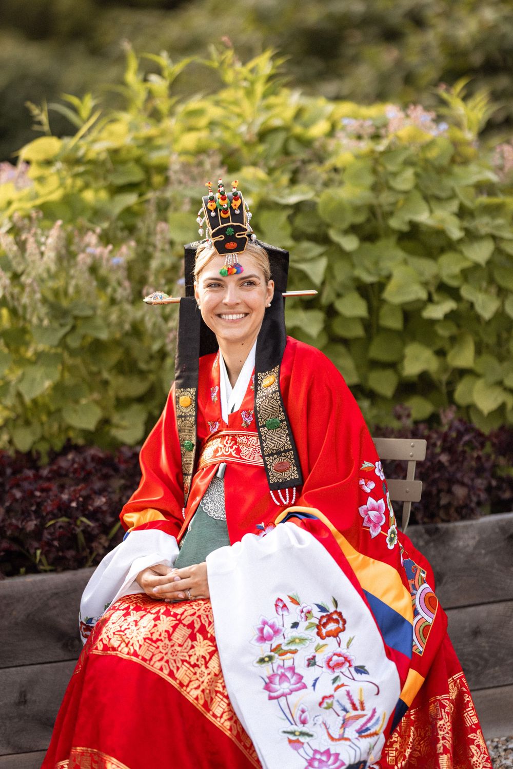 Traditional Korean hanbok dress being worn while holding embroidered artwork in an outdoor garden setting.