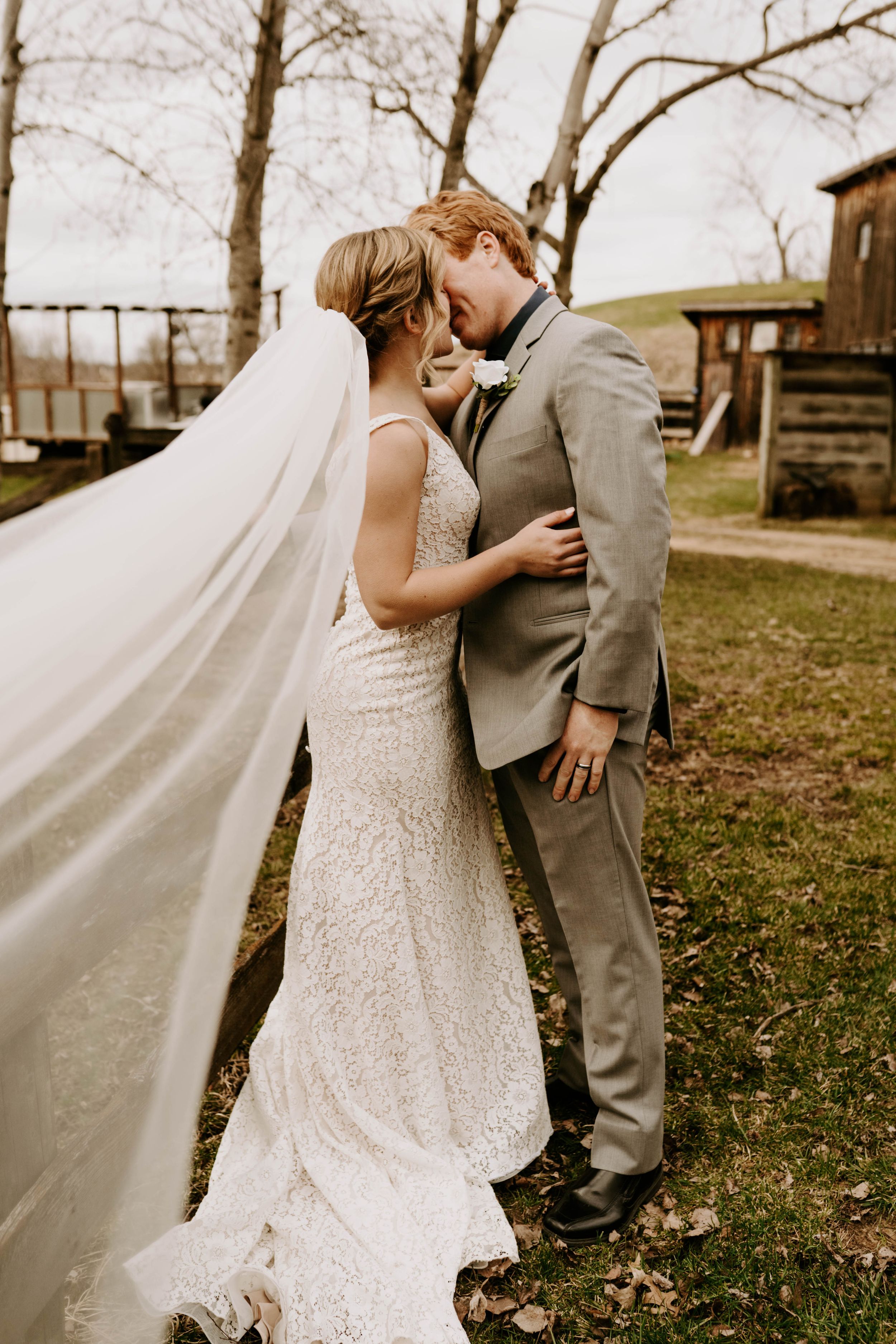 Romantic wedding portraits captured in rustic outdoor setting with vintage barn in background.