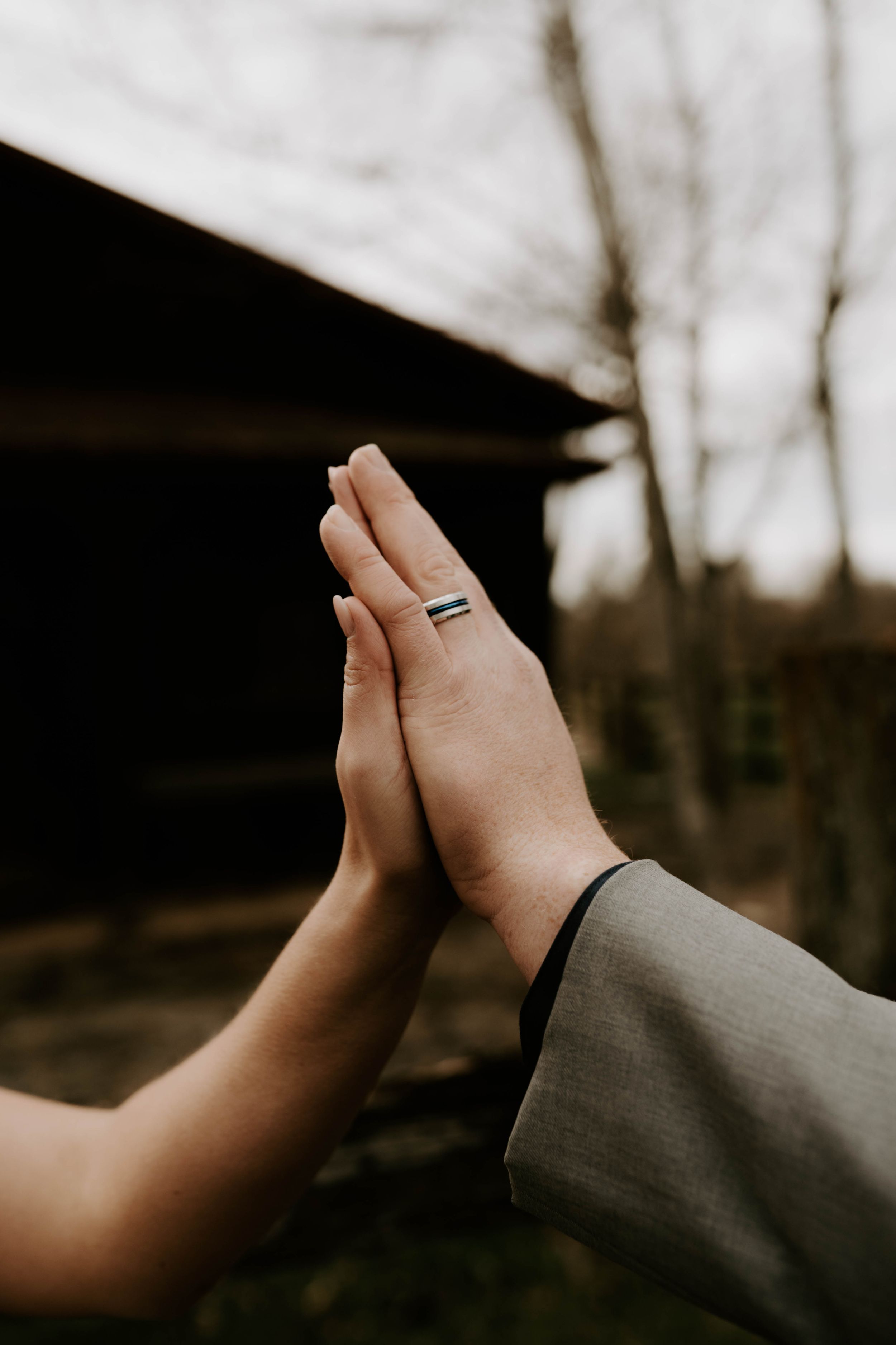 Close-up shot of hands with wedding rings against a moody outdoor background.